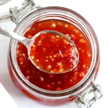 Homemade BEST sweet chili sauce served in a bowl with fresh ingredients around it.