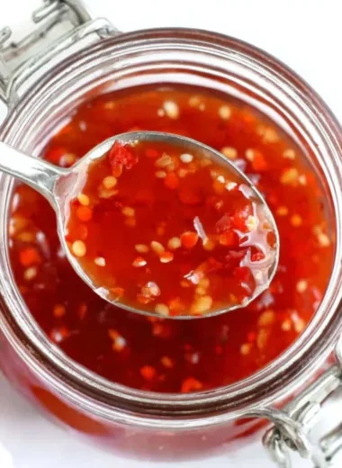 Homemade BEST sweet chili sauce served in a bowl with fresh ingredients around it.