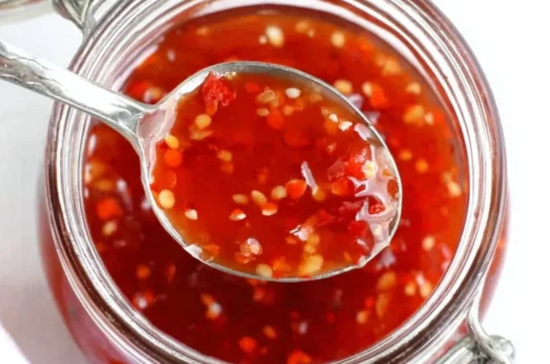 Homemade BEST sweet chili sauce served in a bowl with fresh ingredients around it.