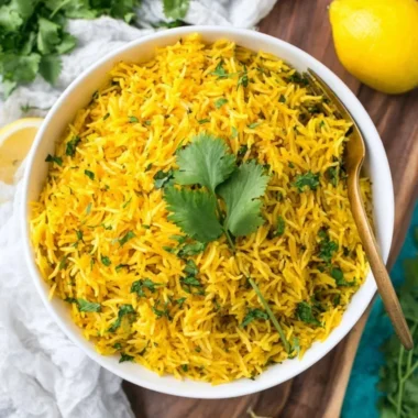 Bowl of vibrant turmeric rice garnished with herbs, showcasing its rich color and texture.