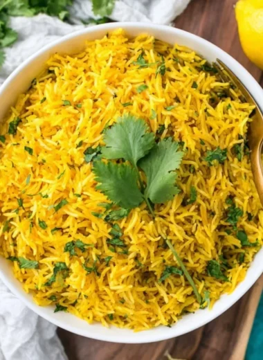 Bowl of vibrant turmeric rice garnished with herbs, showcasing its rich color and texture.