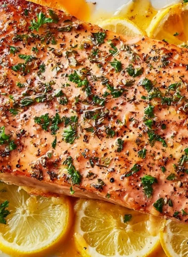 Healthy baked salmon in foil on a plate garnished with herbs and lemon.